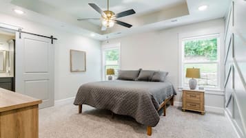 A bedroom with a bed, a nightstand, a dresser, a ceiling fan, and a window with a view of greenery.
