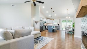 Uma sala de estar moderna com um sofá, um ventilador de teto e uma cozinha ao fundo.