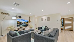 Een moderne woonkamer met grijze banken, een flatscreen televisie, een gitaar en decoratieve muurkunst.