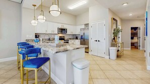 A modern kitchen with white cabinets, a central island with bar stools, stainless steel appliances, and pendant lighting. - Exclusive Gulf view 3BR, pool & tennis (Miramar Beach)