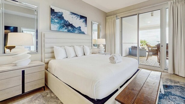 A spacious hotel room with a large bed, a ceiling fan, a view of the outdoors through a sliding glass door, and a painting on the wall. - Exclusive Gulf view 3BR, pool & tennis (Miramar Beach)