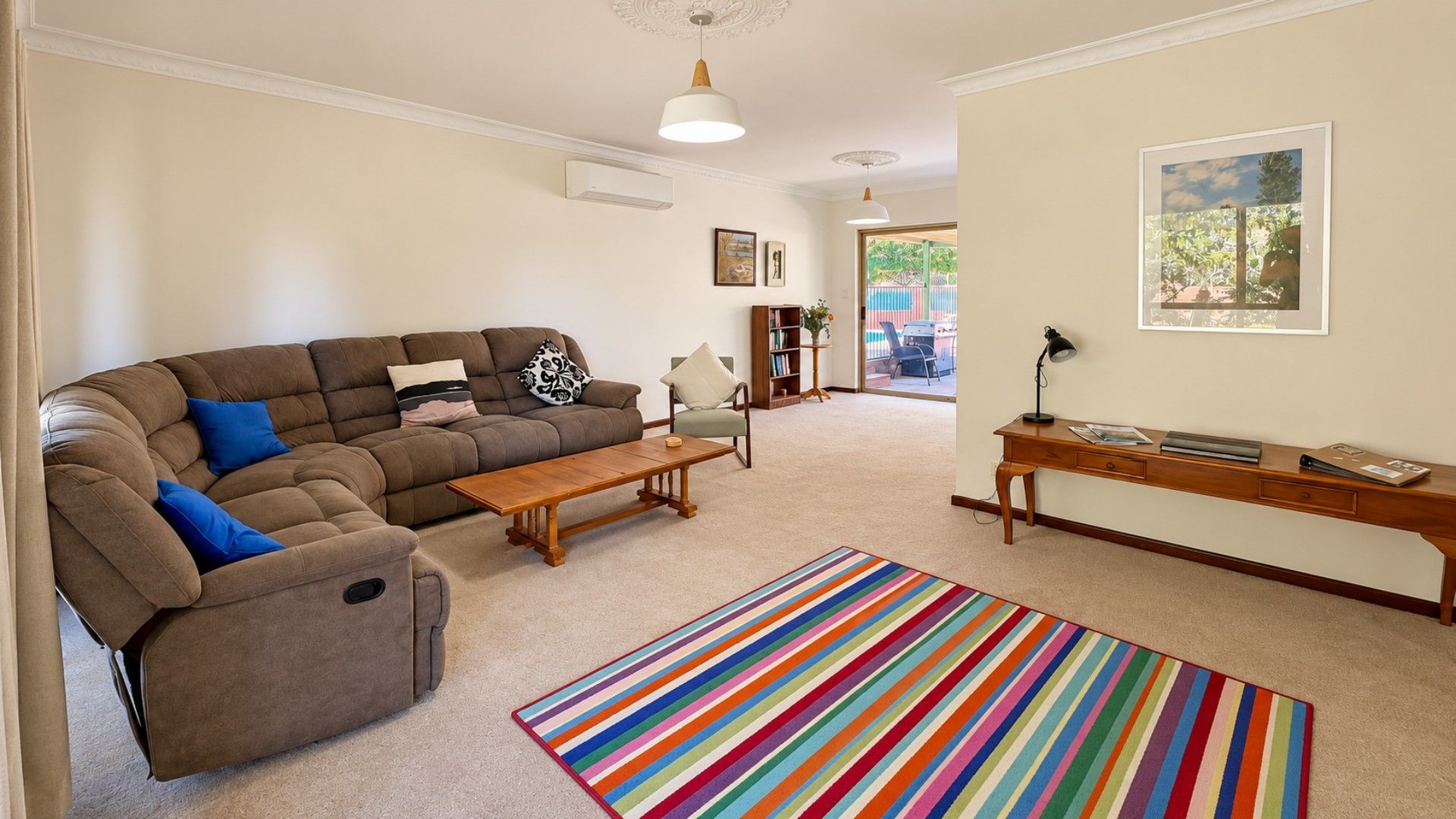 A living room with a sectional sofa, a coffee table, a desk with a lamp, and a colorful striped rug.