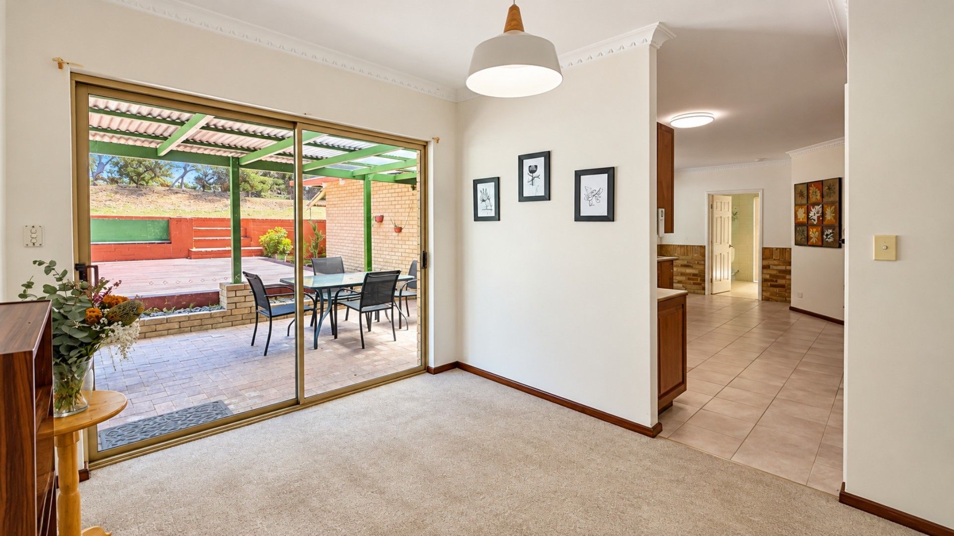 A room with a sliding glass door leading to an outdoor patio, a dining area with chairs and a table, and a kitchen area with cabinets and a countertop.