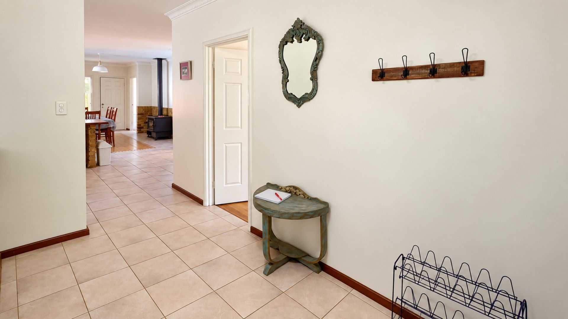 A hallway with a tiled floor, a small table with a notebook, a coat rack, and a mirror on the wall.