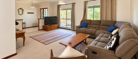 Una sala de estar con sofá, mesa de centro, televisor y ventana con cortinas.
