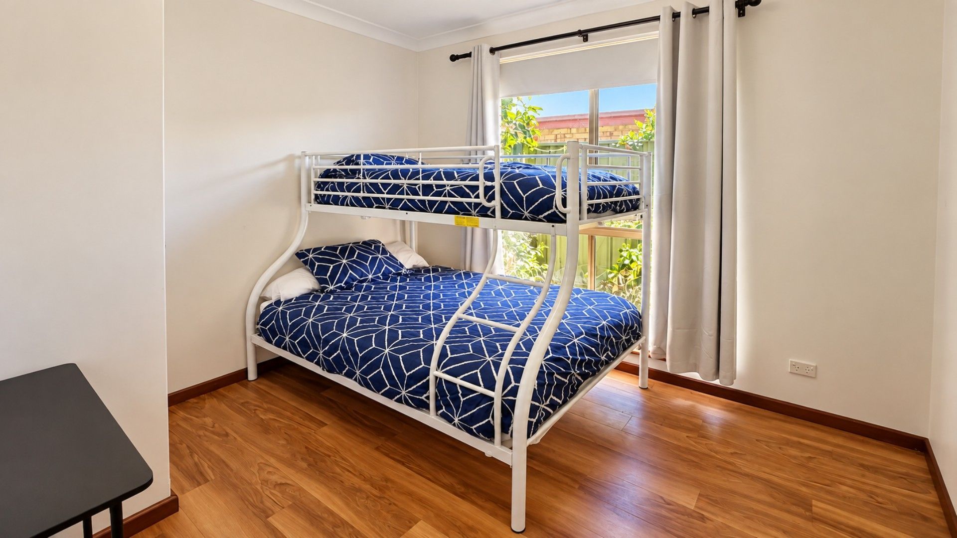 A bunk bed with a geometric patterned bedspread, a small table, and a window with curtains.