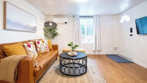 Ein Wohnzimmer mit einem braunen Ledersofa, einem runden schwarzen Couchtisch und einem großen Fenster mit weißen Vorhängen.