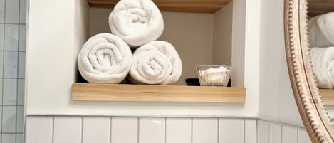 A bathroom with a wooden shelf holding rolled towels and a glass bowl with a bar of soap.