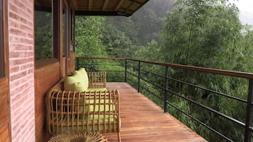 A wooden deck with wicker furniture and a railing overlooking a lush green forest.