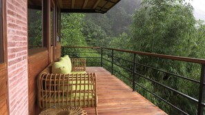 A wooden deck with wicker furniture and a railing overlooking a lush green forest.