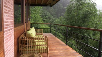 Una terraza de madera con mobiliario de mimbre y barandilla con vistas a un exuberante bosque verde.