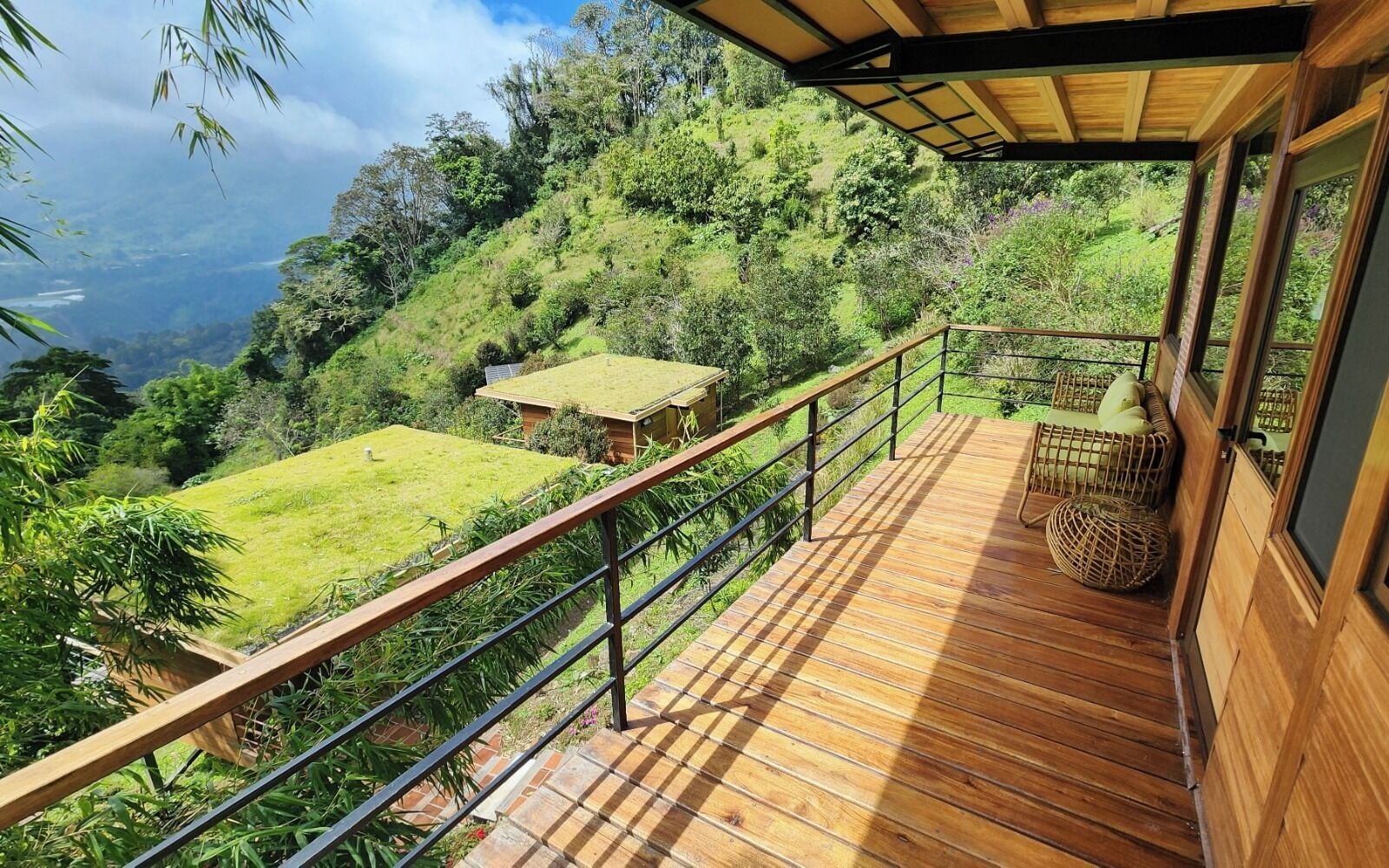 A wooden deck with a railing overlooking a lush green landscape and a small building.
