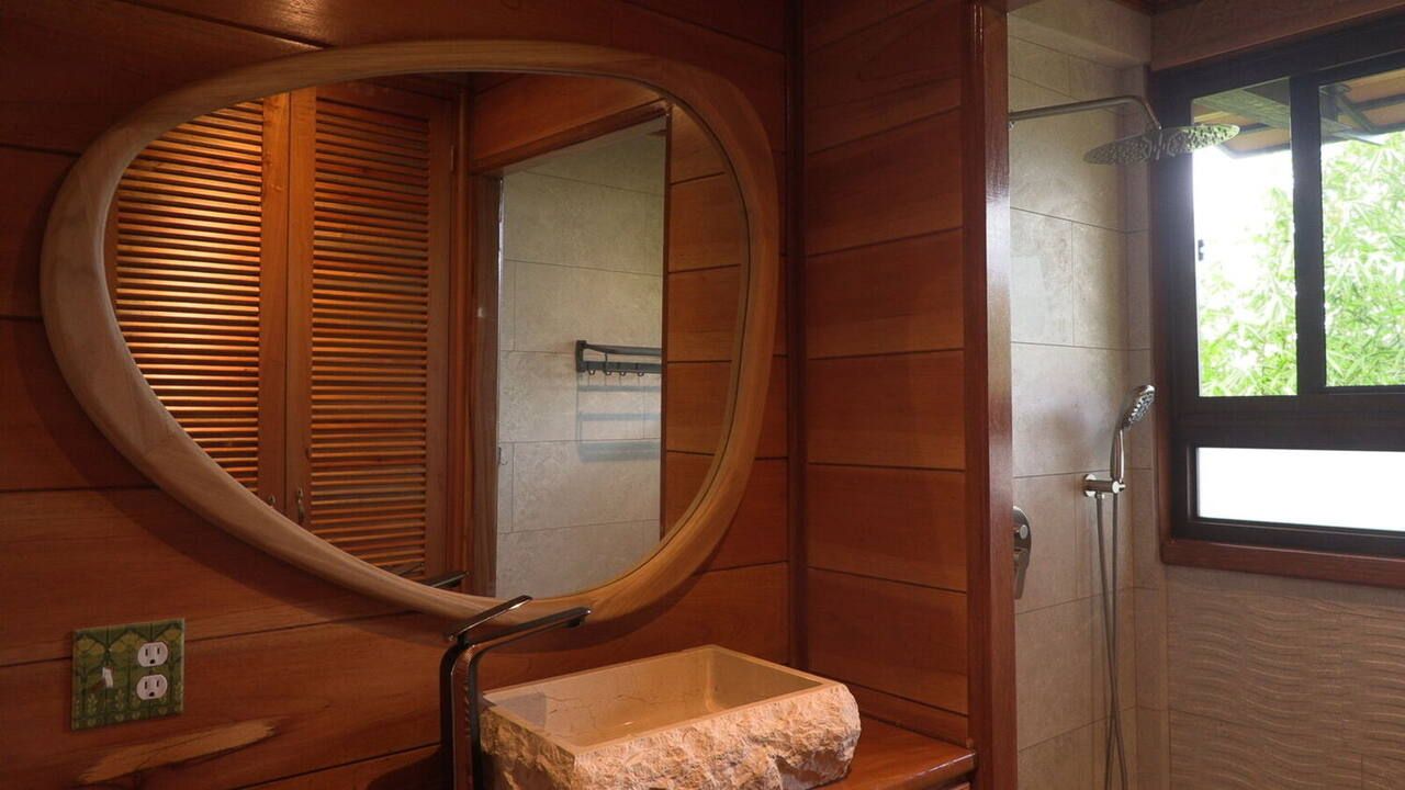 A bathroom with a wooden vanity, a round mirror, and a shower area.