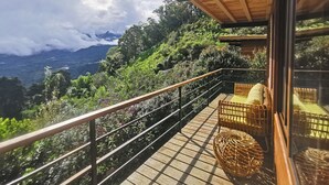 A balcony with wicker furniture, a wooden railing, and a view of a mountainous landscape.