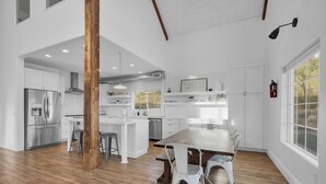 Une cuisine moderne avec des meubles blancs, une table à manger en bois et une grande fenêtre.