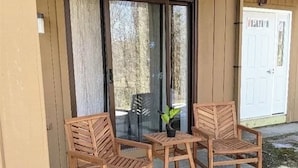 A patio with two wooden chairs and a table, a sliding glass door, and a white door in the background. - Chic ski-in ski-out slopeside 1 bedroom condo at Holiday Valley resort sleeps 4. (Great Valley)