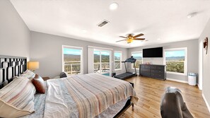 A bedroom with a bed, a treadmill, a TV, and a balcony with a view.