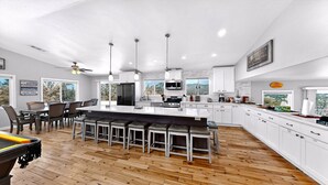 Una cocina moderna con una isla grande, muebles blancos y una zona de comedor con taburetes de bar.