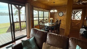A wooden cabin with a dining area, a living room with a sofa, and large windows overlooking a lake. - Callender Blue, a cozy lakeside cabin paradise (Callender Lake)