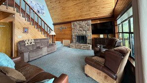 A spacious living room with a stone fireplace, wooden ceiling, and a large window. - Callender Blue, a cozy lakeside cabin paradise (Callender Lake)