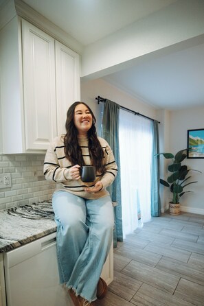 A person sitting on a kitchen counter, holding a mug. - Meridian Suite at North Star Lodge • HotTub • View (Anchorage)