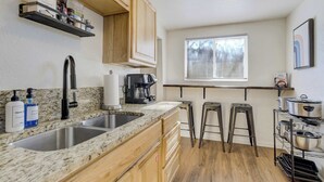 Cocina con encimeras de granito, armarios de madera, pileta doble, cafetera y ventana con persianas.