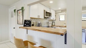 A modern kitchen with white cabinets, a wooden countertop, and a microwave. There are two chairs and a sign that reads "Welcome to Colorado Springs Friends." - Ivywild Flat! Pet Friendly Near Broadmoor w/ Views (Colorado Springs)