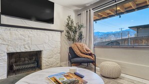 A living room with a stone fireplace, a round coffee table with magazines, a remote control, and a view of a mountain through a large window. - Ivywild Flat! Pet Friendly Near Broadmoor w/ Views (Colorado Springs)