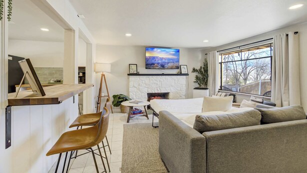A modern living room with a fireplace, a television mounted above it, and a large window. - Ivywild Flat! Pet Friendly Near Broadmoor w/ Views (Colorado Springs)