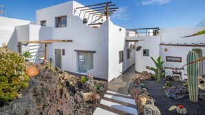 Un edificio moderno blanco con un patio que incluye rocas, plantas y un cactus.