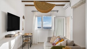 Ett vardagsrum med en tv, en vävd hängande lampa, en soffa och utsikt över havet genom ett fönster.