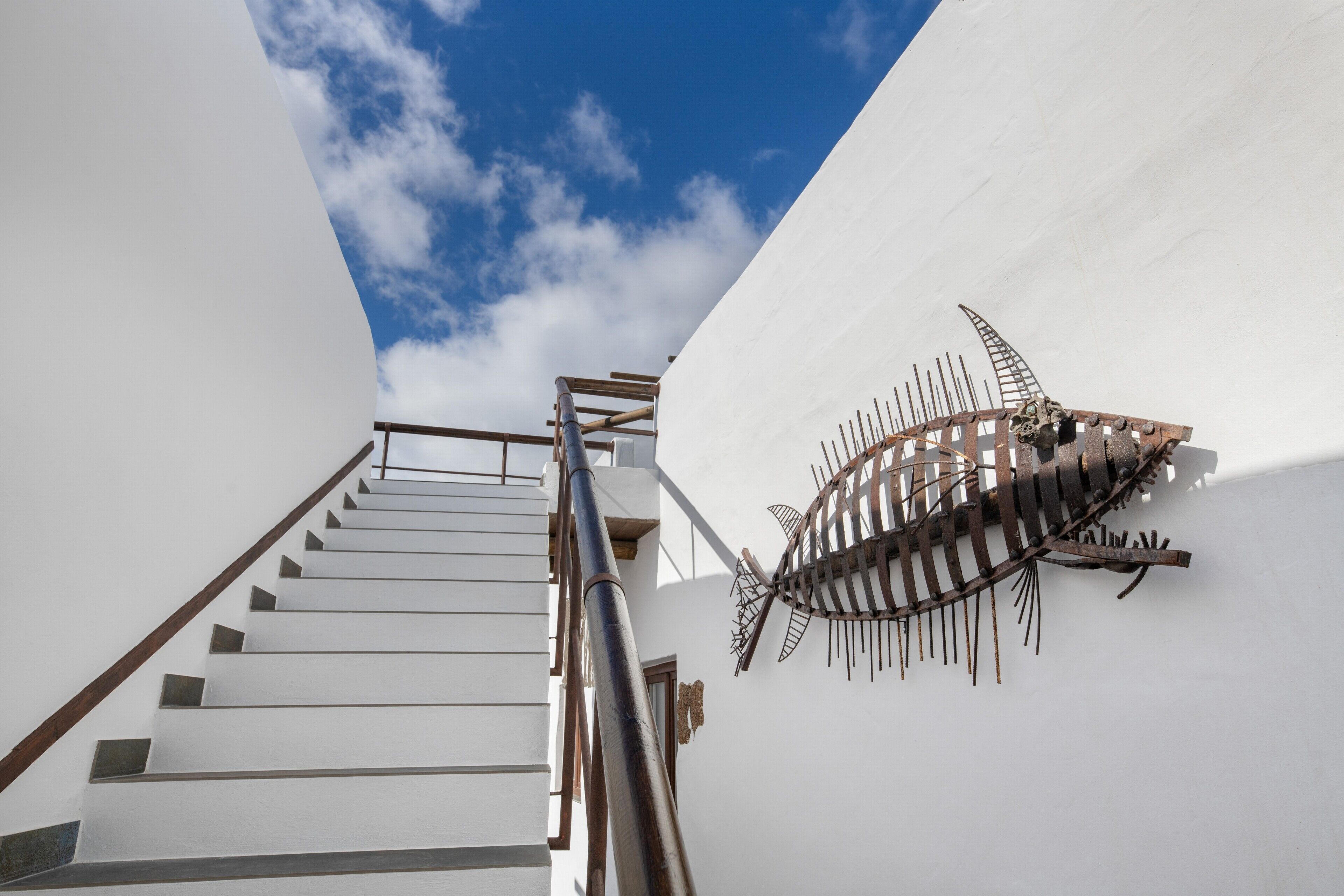 A staircase leading up to a white building with a metal fish sculpture on the wall.