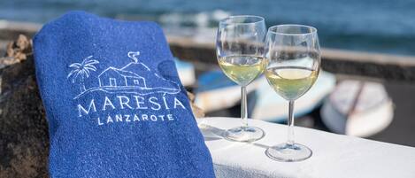 Una toalla con el texto 'MARESIA LANZAROTE', dos vasos de vino blanco y vista al mar.