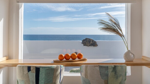 A room with a view of the sea, a wooden table with oranges, a cactus, and a vase with dried plants. - Vacation Apartment 'Maresía' with Sea View, Wi-Fi and Air Conditioning (Haría)