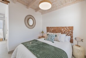 Een slaapkamer met een bed, een houten hoofdbord, een spiegel aan de muur, een bedlampje en een kleine houten sculptuur van een vis.