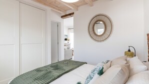 A bedroom with a bed, a circular mirror, a bedside lamp, and a door leading to another room. - Vacation Apartment 'Maresía' with Sea View, Wi-Fi and Air Conditioning (Haría)