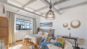 A bedroom with a large bed, a sofa, a dining table, and a view of the sea. - Vacation Apartment 'Rumor del Mar' with Sea View, Wi-Fi and Air Conditioning (Haría)