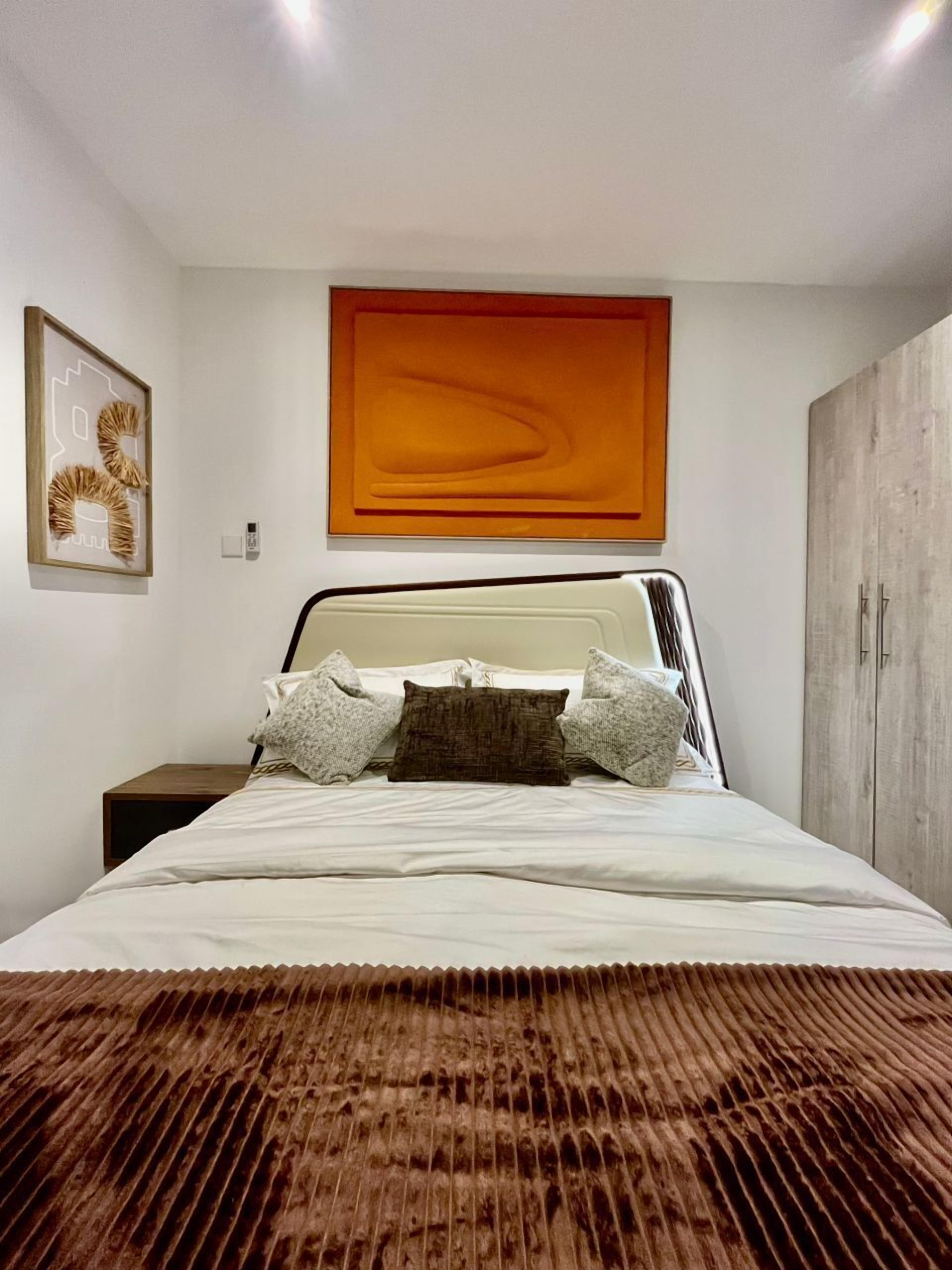 A bedroom with a bed, a nightstand, a wardrobe, and a framed artwork on the wall.