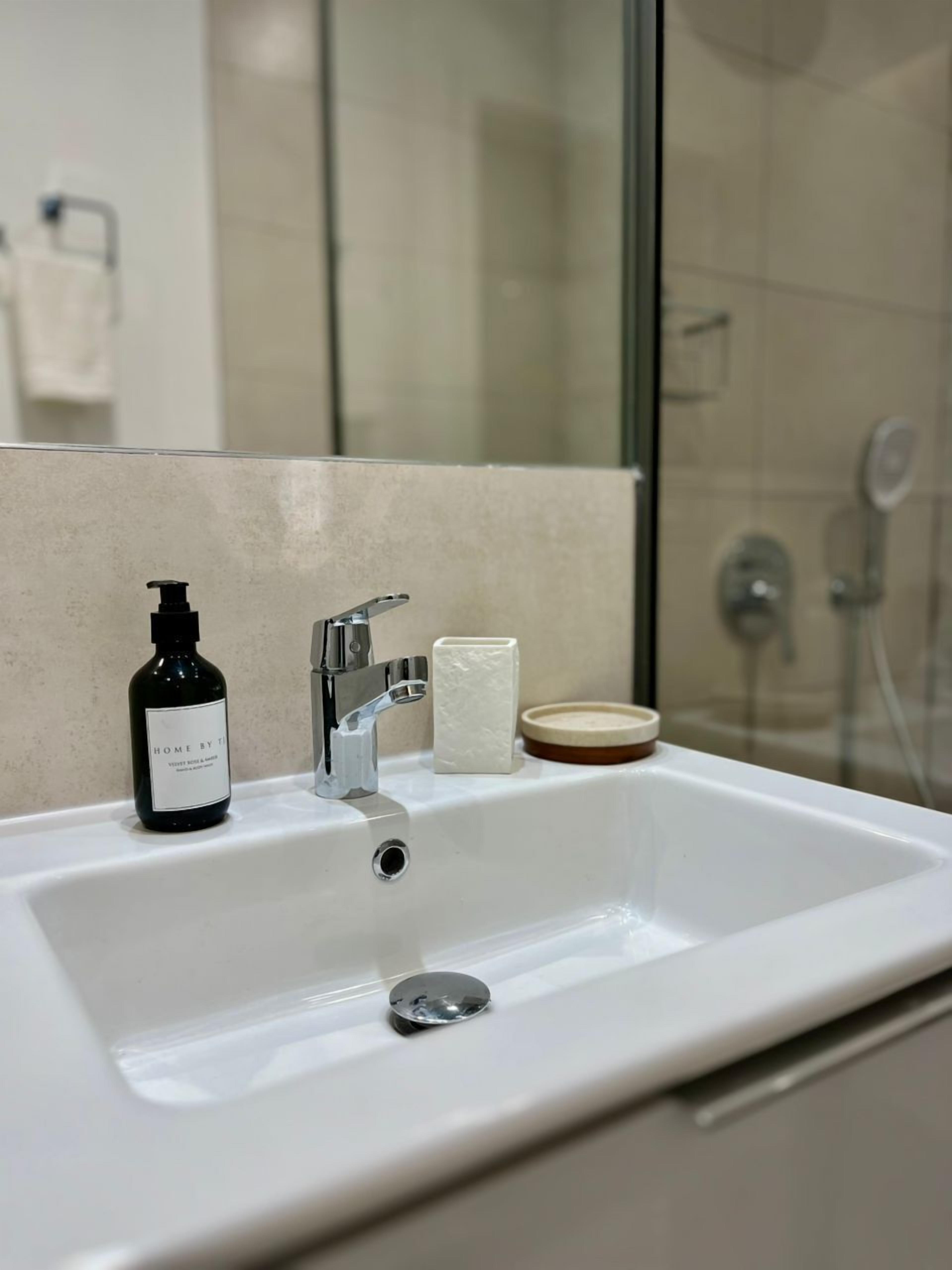 A bathroom with a white sink, a black bottle of soap, a white bar of soap, and a wooden soap dish.