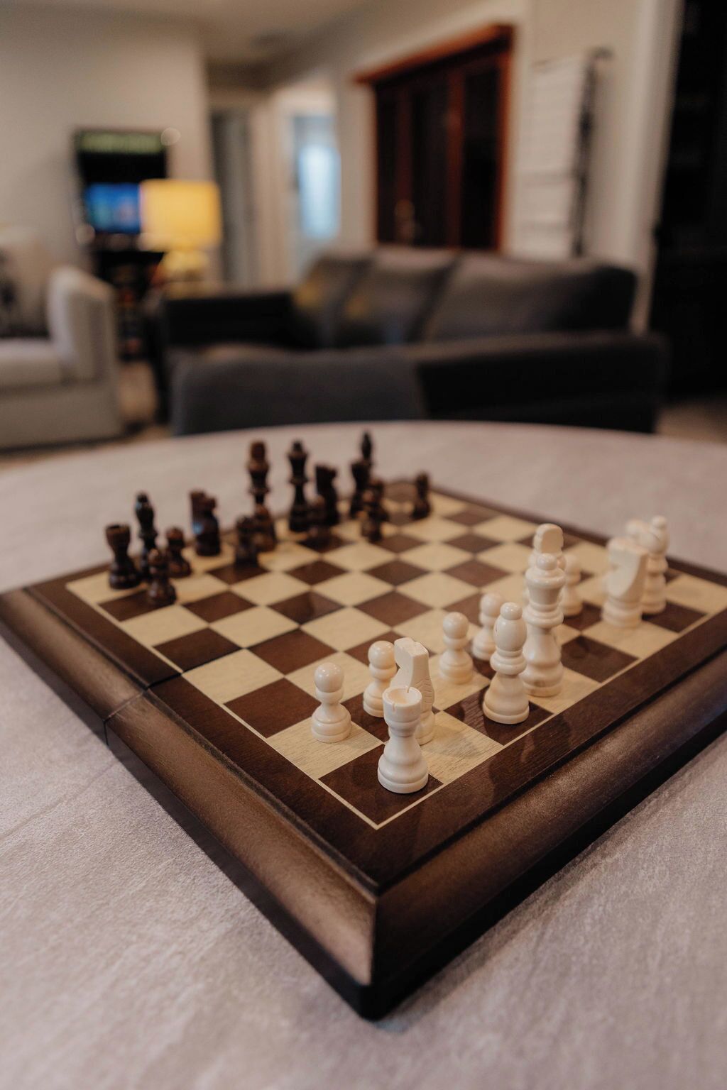 Un tablero de ajedrez sobre una mesa en una sala de estar, con un sofá y una televisión al fondo.
