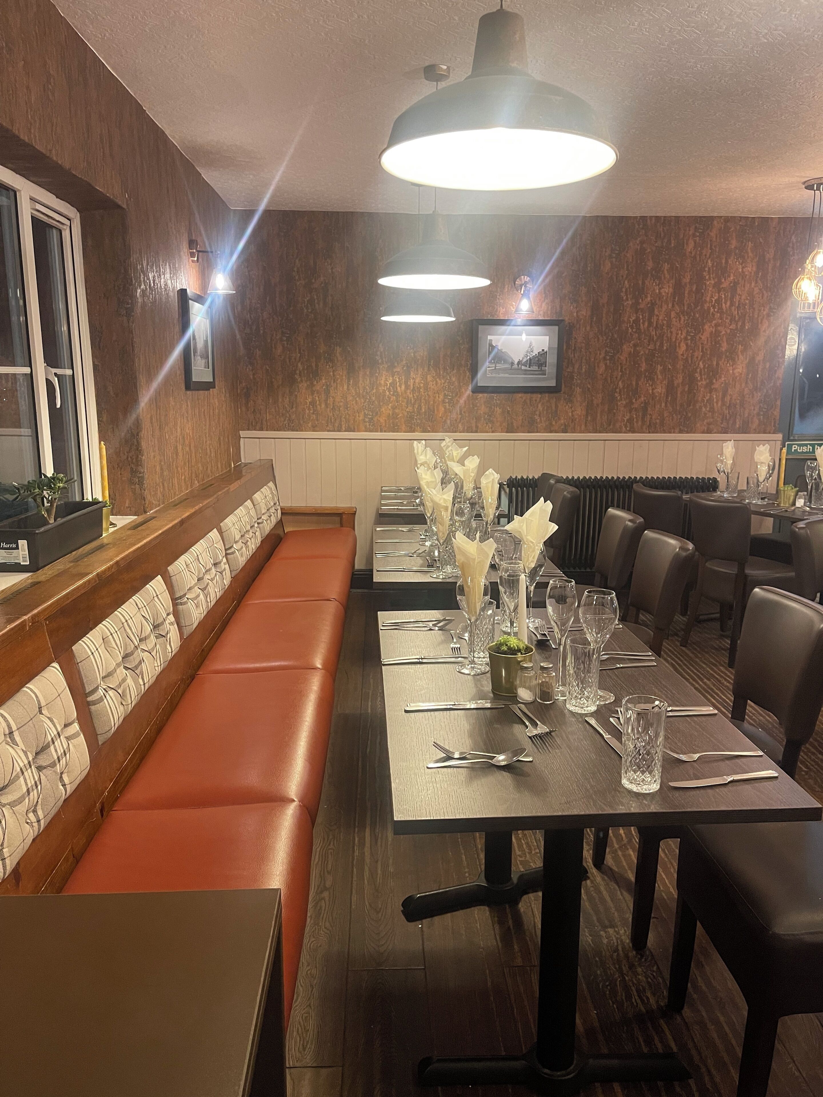 Un restaurante con un banco de madera largo, una mesa con cubiertos, vasos y un jarrón de flores.