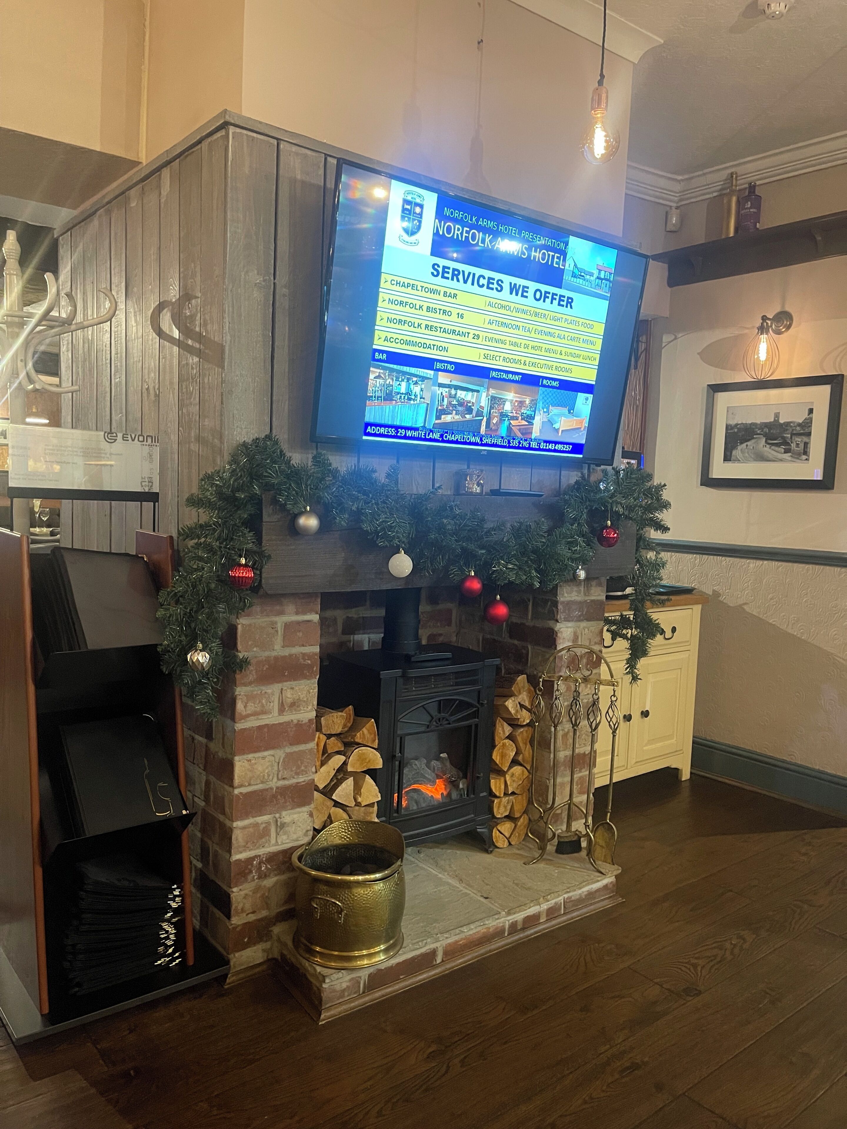A fireplace with a TV displaying a hotel presentation, a brick wall, and a Christmas tree.