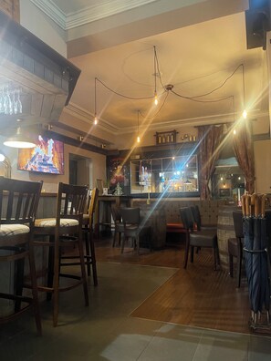 Zona de bar con sillas de madera, un televisor mostrando una escena de fuego y un letrero navideño.
