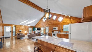 A spacious kitchen with wooden cabinets, a large island with stools, and a high ceiling with skylights. - Cozy Cabin in Mountains | Firepit | Views | Games (Helen)