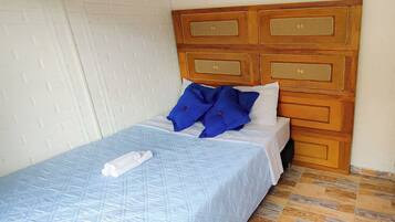 Una cama bien hecha con colcha azul, un cabecero de madera con cajones y una pared con diseño de ladrillos blancos.