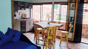 A room with a bed, a dining table with chairs, a kitchen area, and large windows.