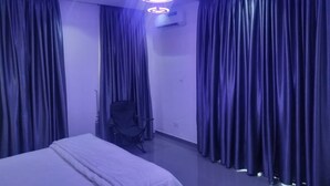 Quarto de hotel moderno com cama, cortinas escuras, luminária no teto e uma cadeira.