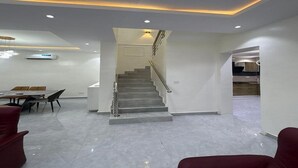 Um interior moderno com uma escada que dá para um segundo andar, uma sala de jantar com mesa e cadeiras, e uma cozinha visível por uma porta aberta.