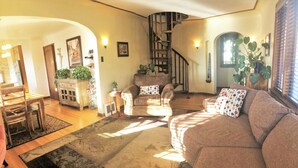 A cozy living room with a brown sofa, a wooden coffee table, and a dining area with a wooden table and chairs. A spiral staircase is visible in the background. - 6-Bedroom Tudor in the Historic District (Salt Lake City)