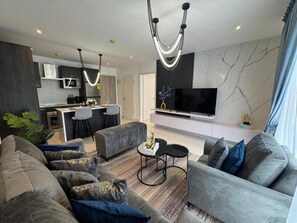 A modern living room with a grey sofa, a coffee table, and a TV on a white entertainment unit. - Loxwood House by Cozy (Accra)